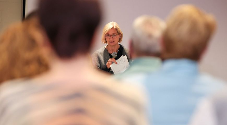 Die saarländische Ministerpräsidentin Anke Rehlinger spricht bei einem Bürgerdialog zum Strukturwandel im Landkreis Merzig-Wadern mit einem Mikrofon zu den Teilnehmerinnen und Teilnehmern. Im Vordergrund sind mehrere Zuhörerinnen und Zuhörer von hinten und unscharf zu sehen; der Blick wird dadurch auf die Rednerin in der Bildmitte gelenkt.